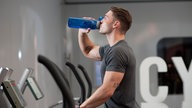 Ein Mann trinkt im Fitnessstudio aus seiner Sportflasche