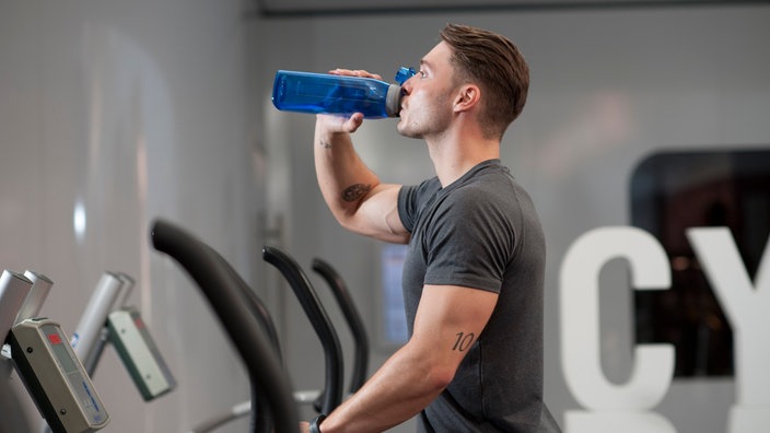 Ein Mann trinkt im Fitnessstudio aus seiner Sportflasche