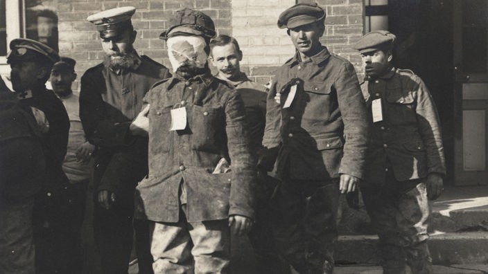 Ein englischer Kriegsgefangener mit einem Gesichtsverband nach einem Gasangriff in Flandern nach 1915, der von einem deutschen Soldaten abgeführt wird (Aufnahmedatum unbekannt)