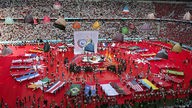 Menschen tragen National-Fahnen auf rotem Grund des Münchner Olympiastadions, Zuschauer 