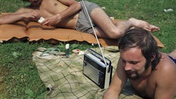 Männer liegen auf einer Decke und hören Radio