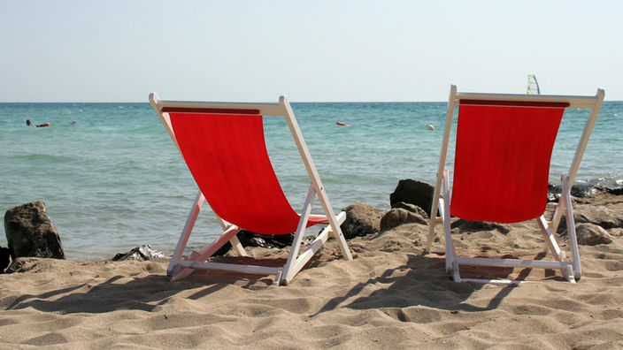 Zwei rote Liegestühle am Strand von Apulien