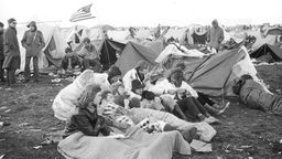 Festival-Besucher in Schlafsäcken vor Zelt auf Wiese 