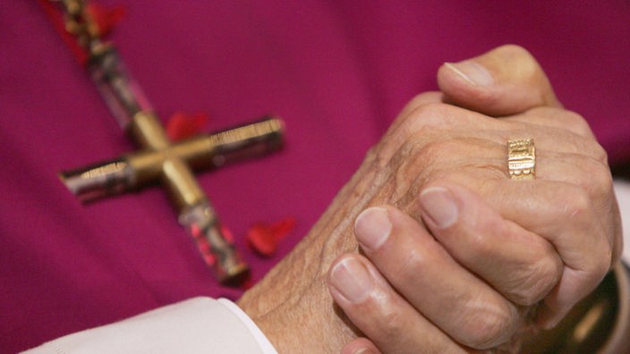 Gefaltete Hände eines Bischofs, der ein Kreuz trägt