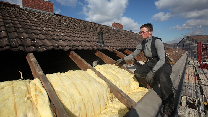 Eine Dachdeckerin verlegt Isoliermaterial auf Hausdach
