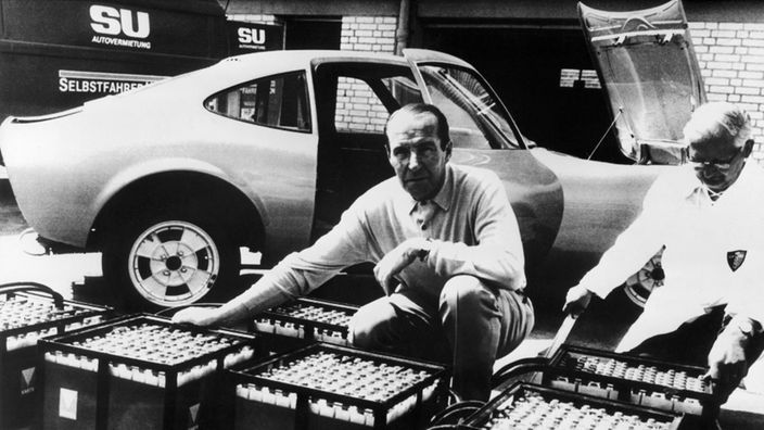 Georg von Opel mit sechs Batterie-Trögen vor Opel GT