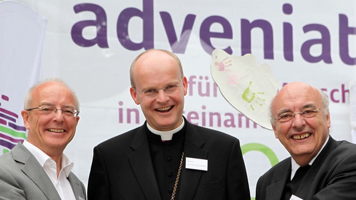 Essens Oberbürgermeister Reinhard Paß, Bischof Franz-Josef Overbeck und Prälat Bernd Klaschka vor Adveniat-Logo