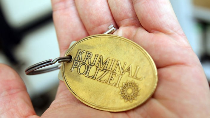 In einer offenen Hand Liegt eine Marke mit der Aufschrift "Kriminalpolizei"