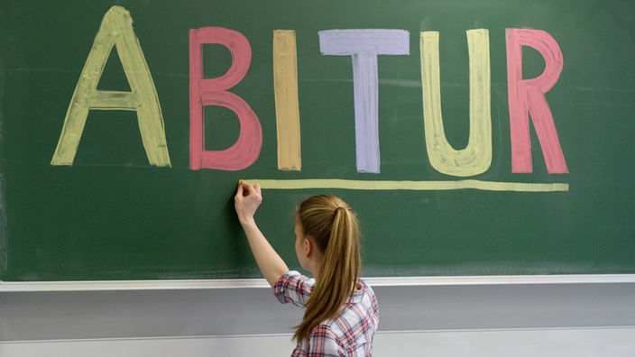 Eine Schülerin schreibt das Wort ABITUR an die Tafel