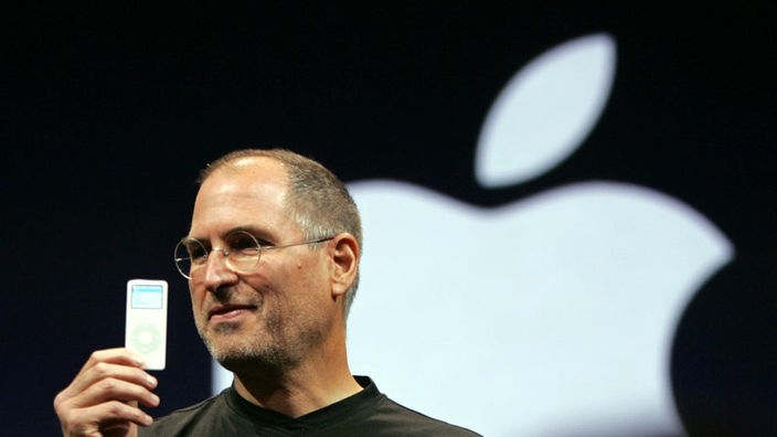 Steve Jobs hält einen iPod hoch, im Hintergrund das Apple-Logo