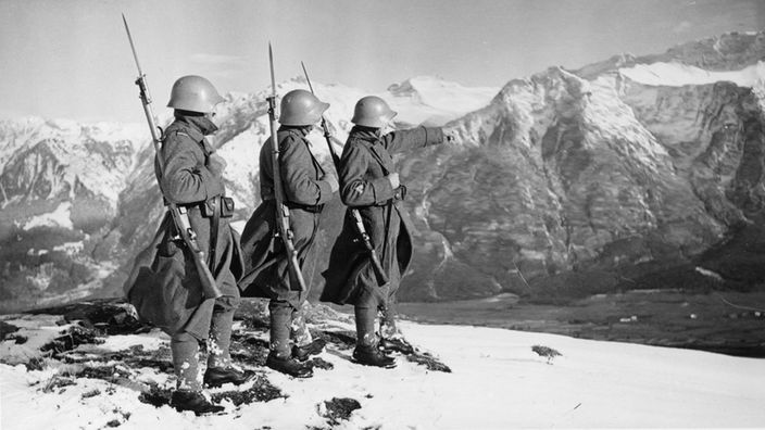 Drei Schweizer Soldaten schauen auf eine Alpenlandschaft (1939)