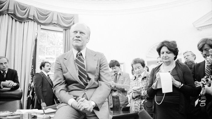 Gerald Ford auf Schreibtisch sitzend bei Pressegespräch im Weißen Haus (30.09.1976)