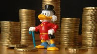 Symbolfoto: Dagobert-Duck-Figur, aufgestappelte Münzen