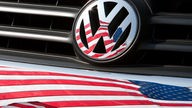 Die US-Fahne spiegelt sich in Logo und Kühlergrill eines Volkswagen-Fahrzeugs