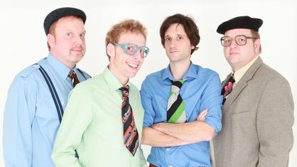 Vier Mitglieder der Band Kapelle Petra posieren mit Hemd und Krawatte für ein Gruppenfoto.