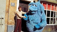 Jim Henson schüttelt einer riesigen, blauen Puppe der "Muppet Show" die Hand