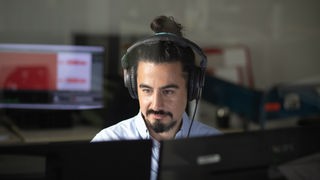 Mann sitzt vor Computer mit Kopfhörern