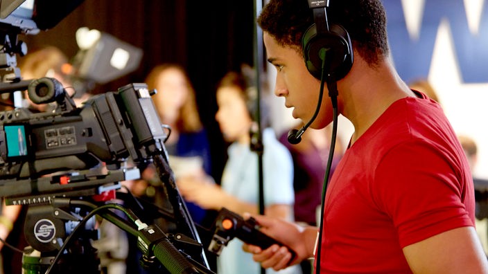 Ein männlicher Jugendlicher mit Headset, bedient eine Fernsehkamera.