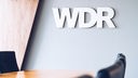 WDR-Logo an einer Wand, davor stehen Besprechungstisch und -stühle