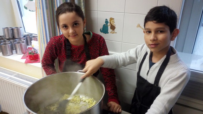 Ein Junge und ein Mädchen stehen vor einem großen Kochtopf