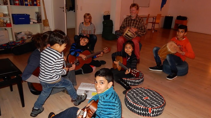 Kinder sitzen im Kreis, spielen Musikinstrumente