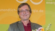 Michael Houben steht mit Blumenstrauß und Urkunde vor dem Logo des Journalistenpreises "Unendlich viel Energie"