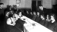 Gruppe Männer und Frauen sitzt am Tisch und hört über Kopfhörer Radio