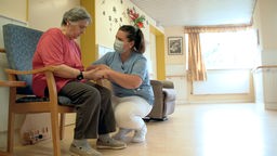 Pflegerin mit einer sitzenden älteren Frau in einem Flur im Pflegeheim