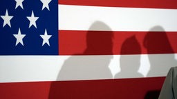Symbolbild: drei menschliche Schatten auf einer US-Flagge.
