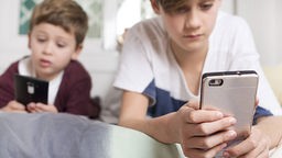 Das Bild zeigt zwei Kinder mit Smartphones in der Hand. 