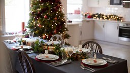 Festlich geschmückter Tisch fürs Weihnachtsessen, im Hintergrund ist ein Weihnachtsbaum