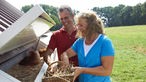 Barbara Büsch steht mit ihrem Mann vor dem Hühnermobil und sammelt Eier ein.