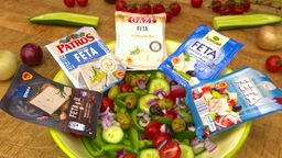Das Bild zeigt Feta-Käse verschiedener Anbieter um eine Salatschüssel herum.
