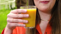 Das Bild zeigteine weiblich gelesene Person, die ein Glas mit Smoothie in der Hand hält.