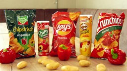 Auf einem Tisch stehen nebeneinander Paprika-Chips-Packungen von den Herstellern funnyfrisch, Gut & Günstig, Lay's, Pringles und Crunchips.