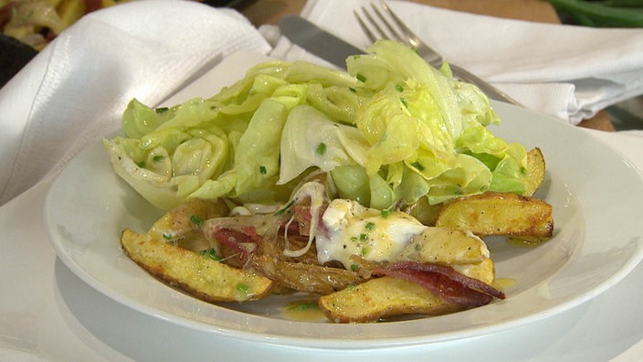 Käsekartoffeln mit Speck und Salat, auf einem Teller angerichtet