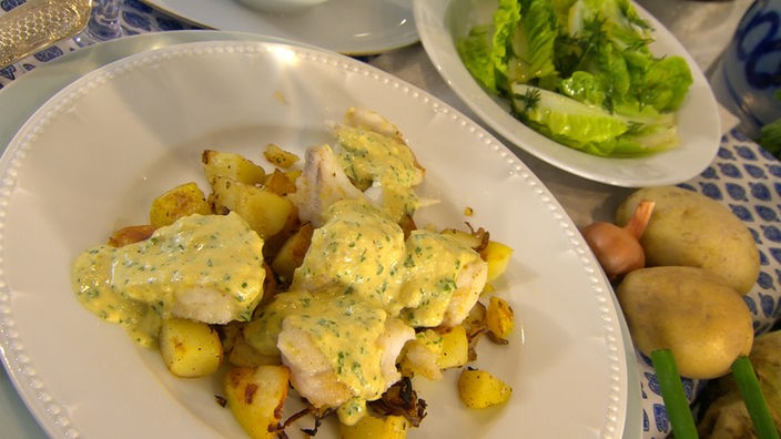 Helgoländer Pannfisch mit Kartoffeln auf einem Teller angerichtet, daneben ein Teller mit grünem Salat