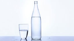 Das Bild zeigt eine Flasche Mineralwasser und ein Glas Wasser.