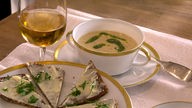 Schwarzbrot-Petersilienwurzel-Cremesüppchen in einer Suppentasse angerichtet, daneben ein Teller mit Schwarzbrot und ein Glas Wein