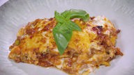 Das Bild zeigt das Gericht "Sizilianische Lasagne" auf einem Teller mit frischem Basilikum präsentiert.