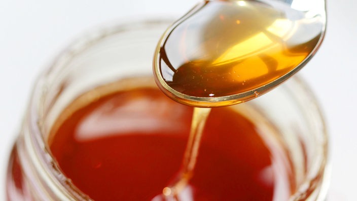 Ein Löffel mit Honig über einem Honigglas.