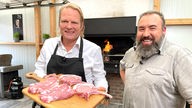 Gemeinsam mit Grillweltmeister und Fleischsommelier Oliver Sievers (r) bereitet Björn Freitag Koteletts und saftige Spareribs auf dem Grill zu.