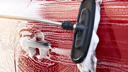 Das Bild zeigt die Reinigung eines roten PKW.