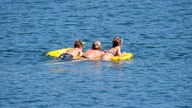Drei Schwimmer auf einer Luftmatratze im Wasser