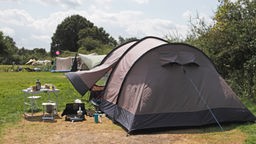 Das Bild zeigt ein aufgebautes Zelt und weitere Camping-Ausrüstung.