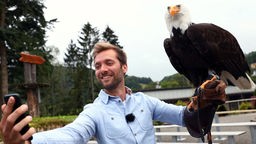 Das Bild zeigt Daniel Aßmann, der ein Selfie mit einem Greifvogel macht.