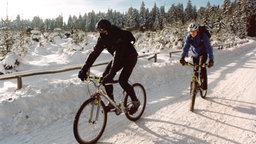 Jugendliche fahren mit ihren Mountainbikes im Schnee.