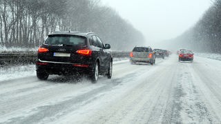 Das Bild zeigt mehrere Autos auf der Autobahn während eines Schneesturms.