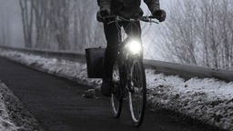 Das Bild zeigt einen Mann auf einem Fahrrad mit Licht bei Dunkelheit.