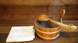 Das Bild zeigt ein Handtuch und einen Holzeimer in einer Sauna.